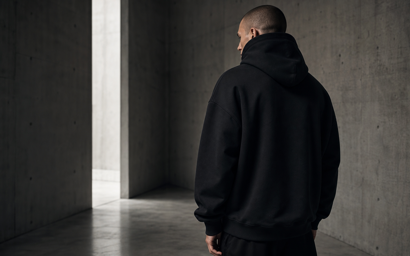 Model in a black hoodie standing in a restrained concrete space